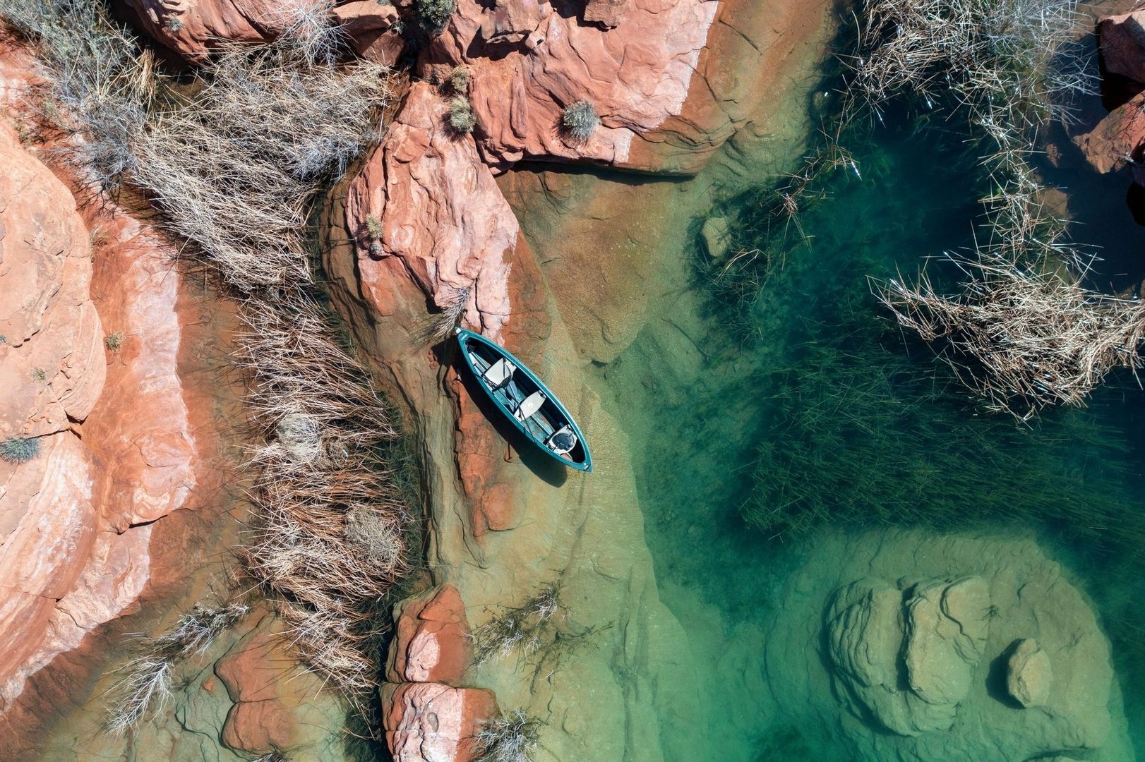 A small kayak floating in clear water beside red desert sandstone
