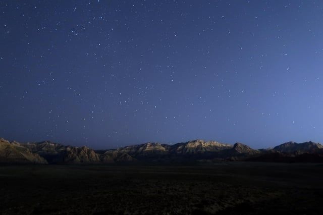 Star-filled night sky above a rugged desert mountain range